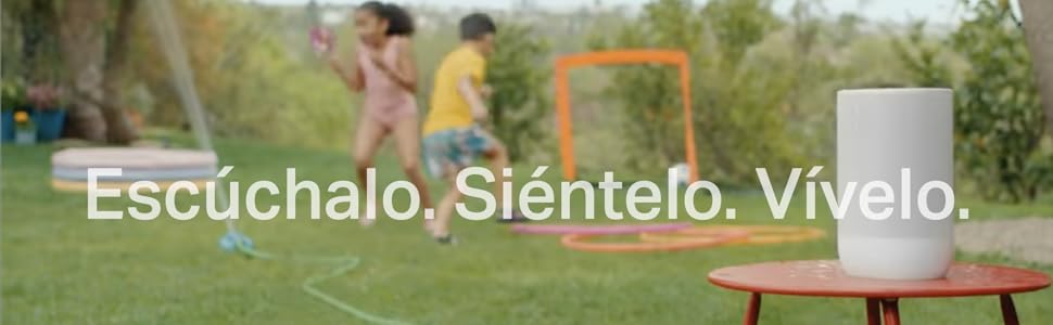 Escena al aire libre con gente jugando de fondo. Mesa naranja en primer plano. Texto en espa&ntilde;ol superpuesto: &laquo;Esc&uacute;chalo. Si&eacute;ntelo. V&iacute;velo. '